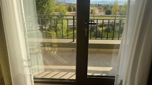 Quarto com porta de vidro deslizante que dá para uma varanda com vista para uma paisagem verde e uma cidade ao longe.