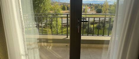 A room with a sliding glass door leading to a balcony with a view of a green landscape and a distant town.