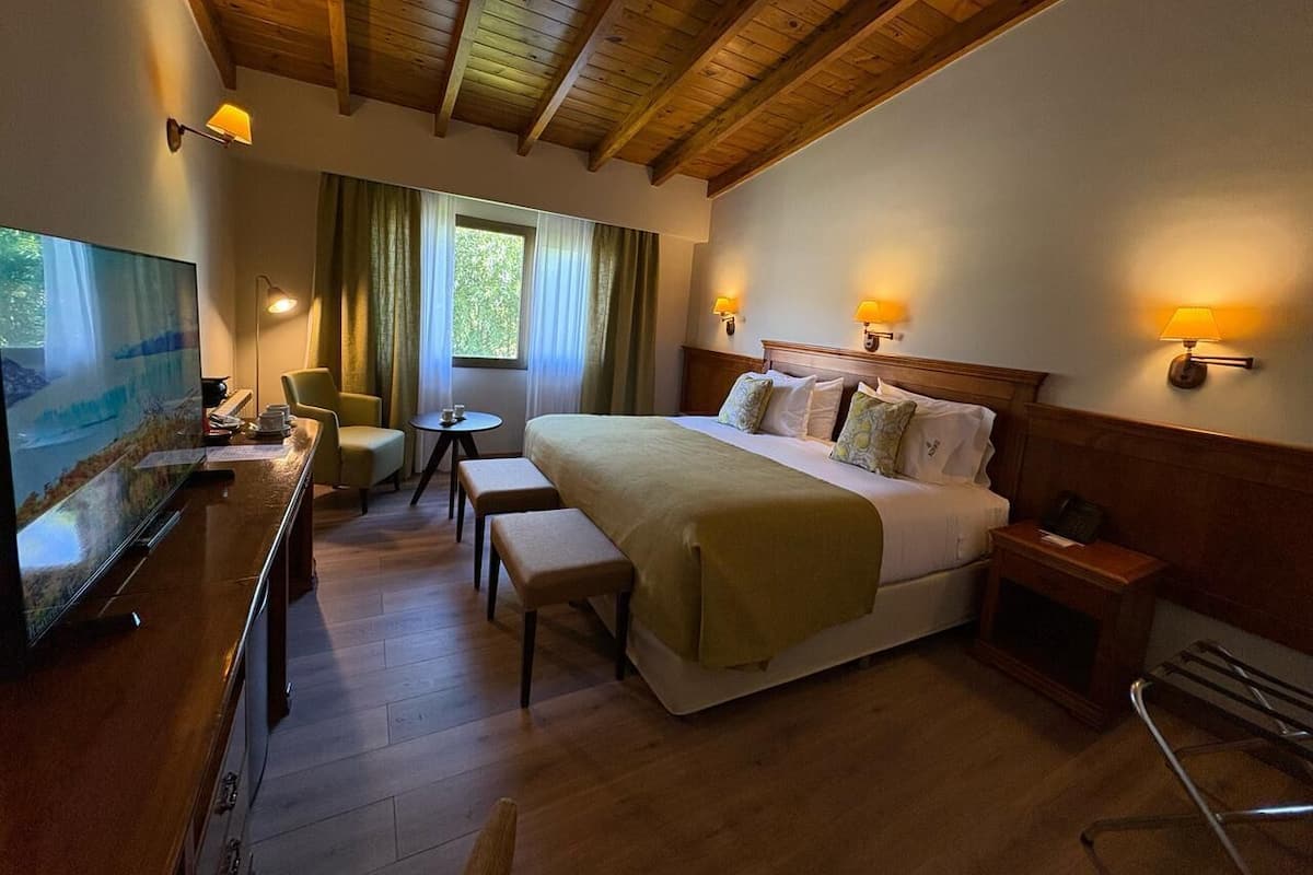 Une chambre d’hôtel avec un grand lit, un bureau avec une télévision, une petite table et un banc.
