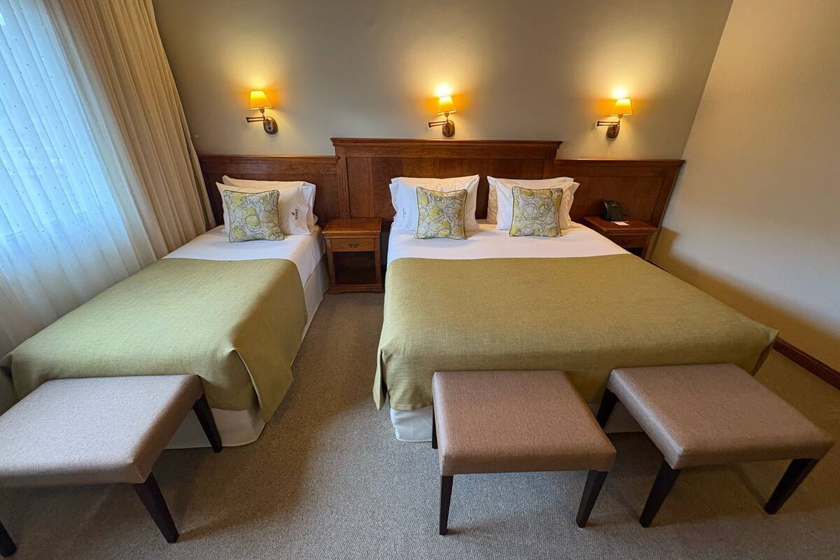Une chambre d’hôtel avec deux lits, chacun étant équipé d’un oreiller et d’une table de chevet. La chambre comprend également deux bancs.