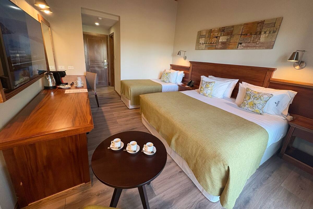 Une chambre d’hôtel avec deux lits, un bureau en bois, une petite table avec des tasses et un tableau au mur.