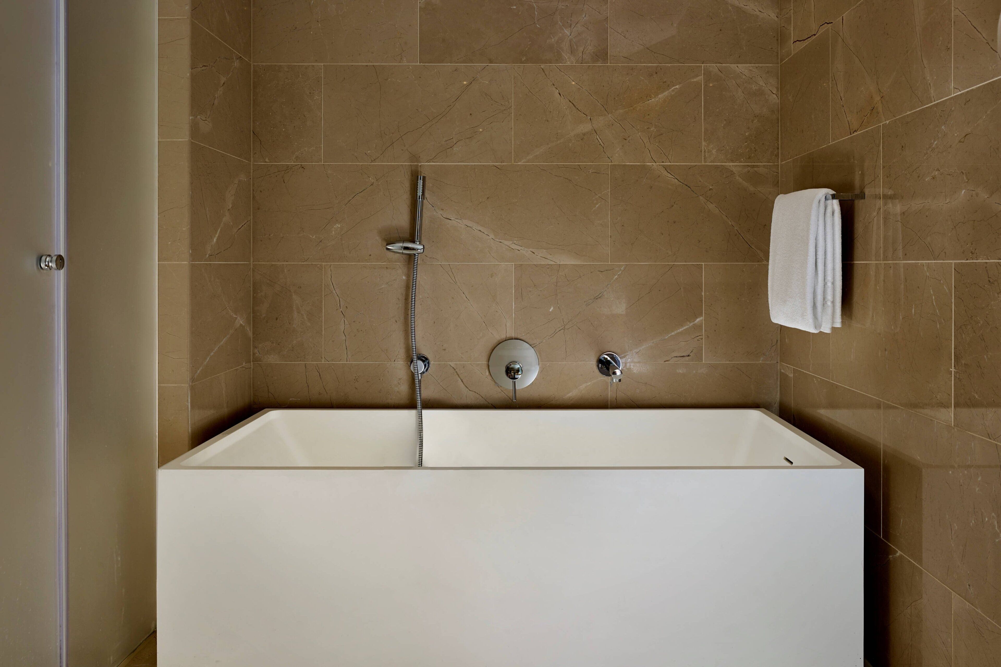 Un baño moderno con una bañera grande, un cabezal de ducha de mano y un perchero para toallas.
