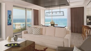 A modern living room with a large window overlooking a beach, a sofa, a coffee table, and a dining area.