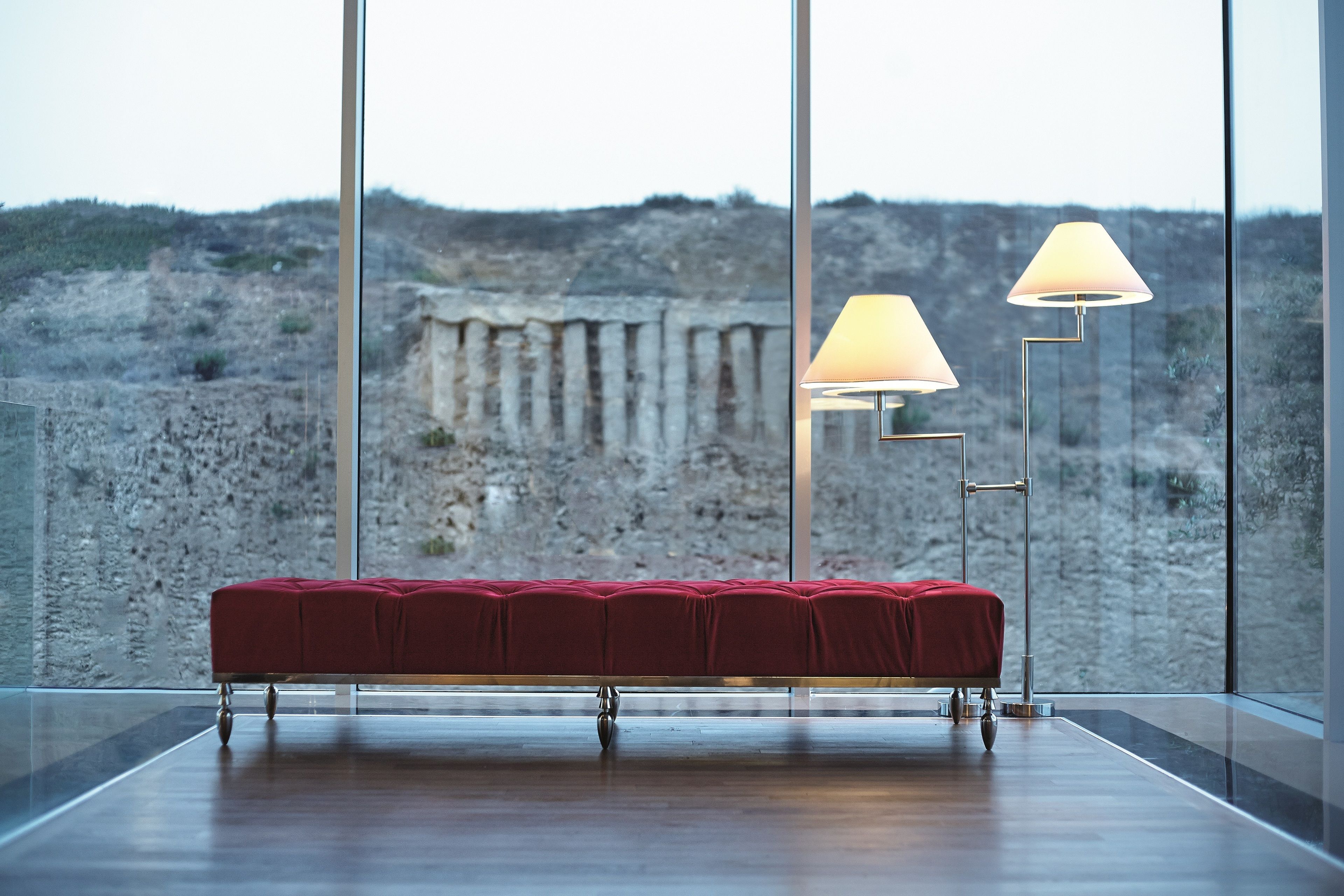 A modern room with a red bench, large windows, and two floor lamps.