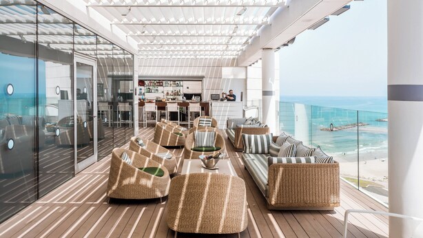 A spacious outdoor lounge area with wicker furniture, a bar, and a view of the ocean.