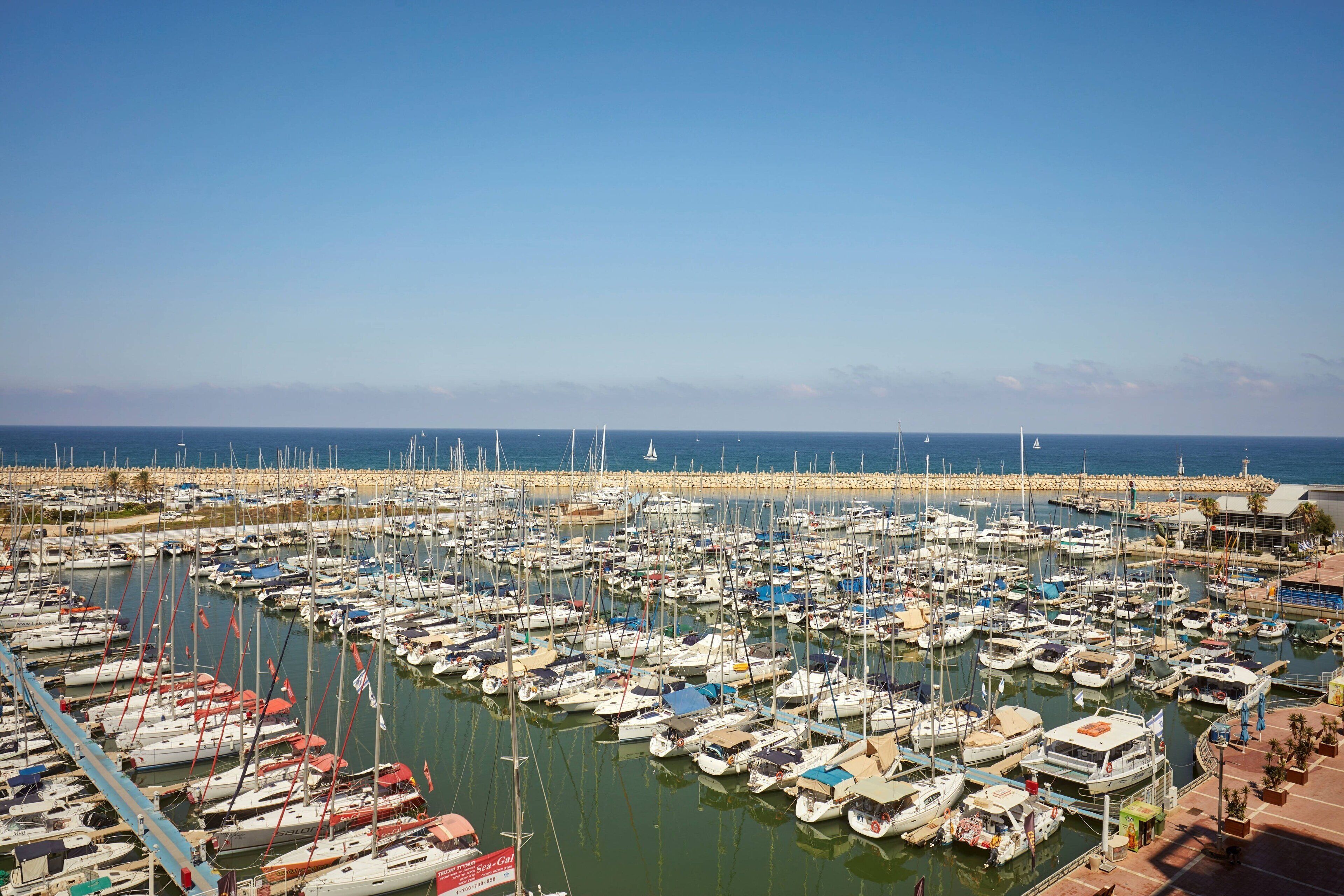 A marina with numerous boats docked, a clear sky, and a calm sea.