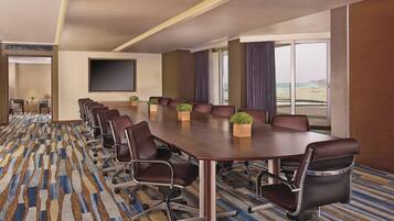 A conference room with a long table, multiple chairs, a large screen, and a view of the beach through large windows.