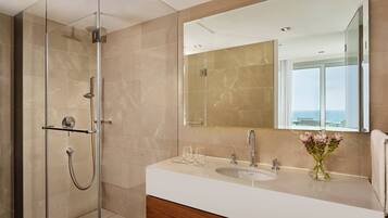 Un baño moderno con cabina de ducha de vidrio, un lavabo blanco y un espejo grande que refleja vistas al exterior.