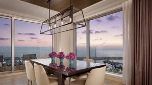 A modern dining area with a glass table, beige chairs, and a view of the sea.