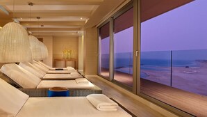 A hotel room with multiple beds, a large window with a beach view, and a wicker headboard.