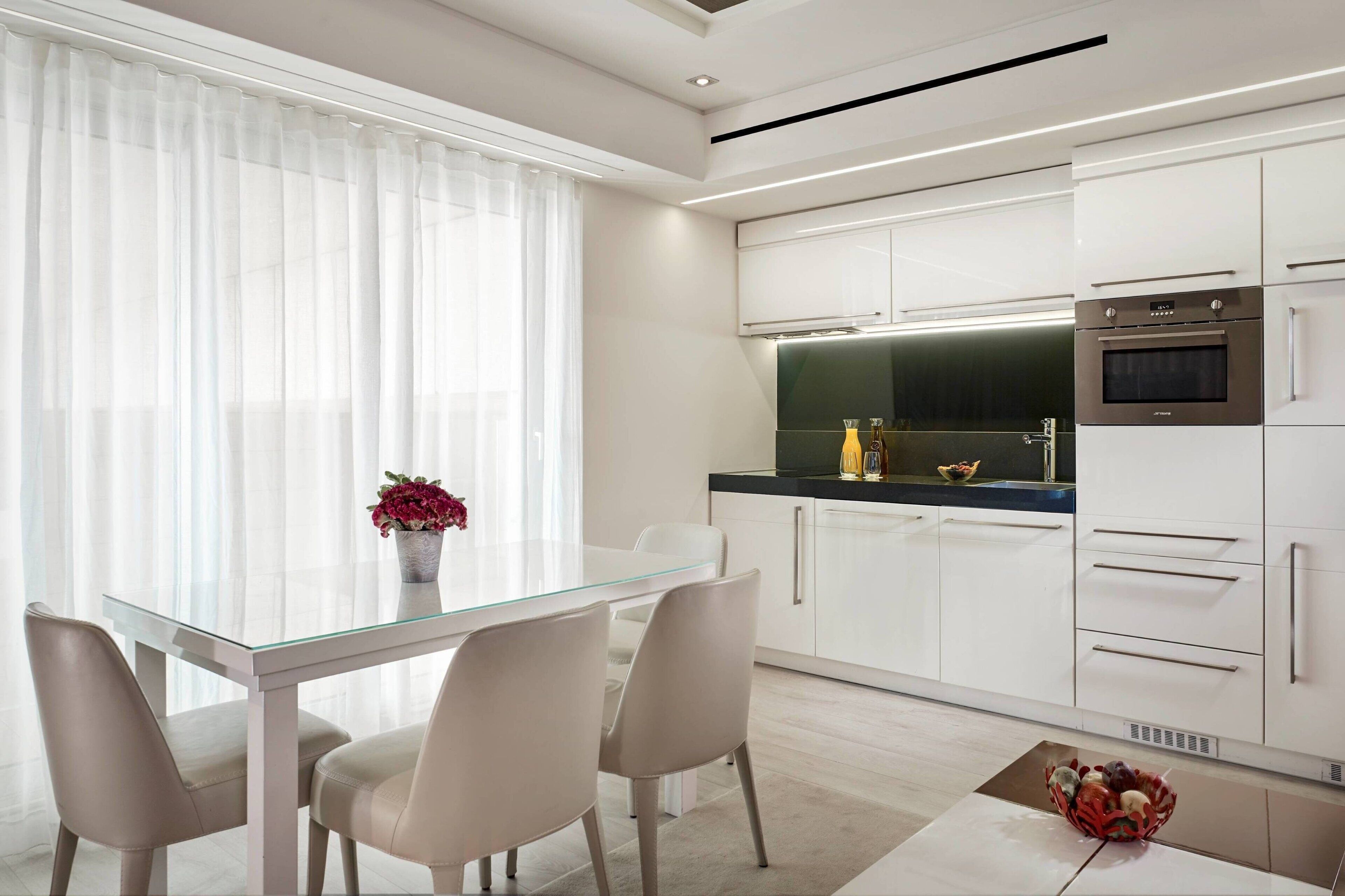 A modern kitchen with white cabinets, a glass dining table, and a built-in oven.