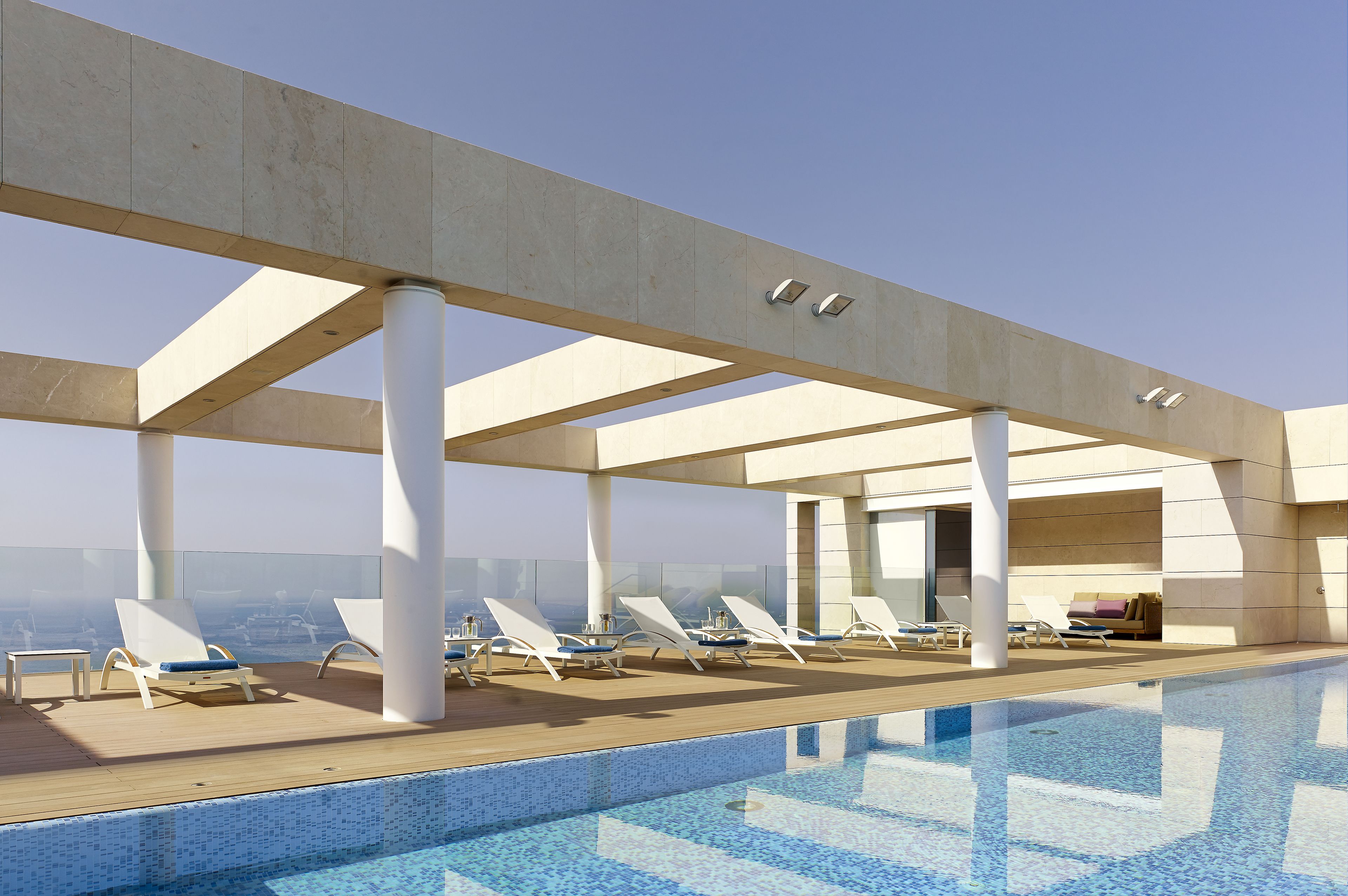 A rooftop pool area with sun loungers and a clear view of the city skyline.