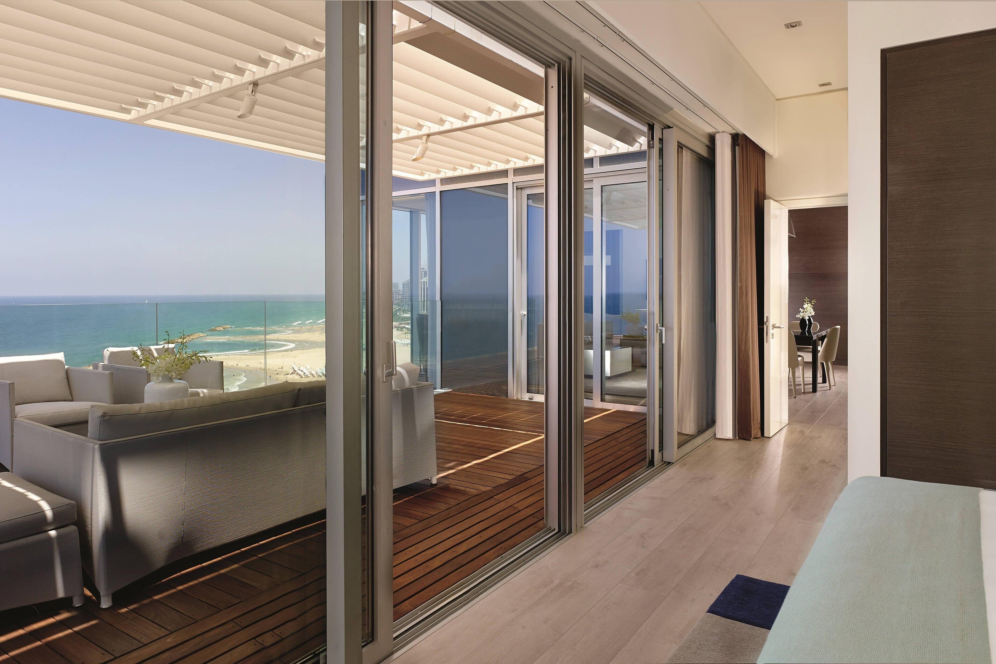 A modern interior with a balcony overlooking a beach, wooden flooring, and a dining area.