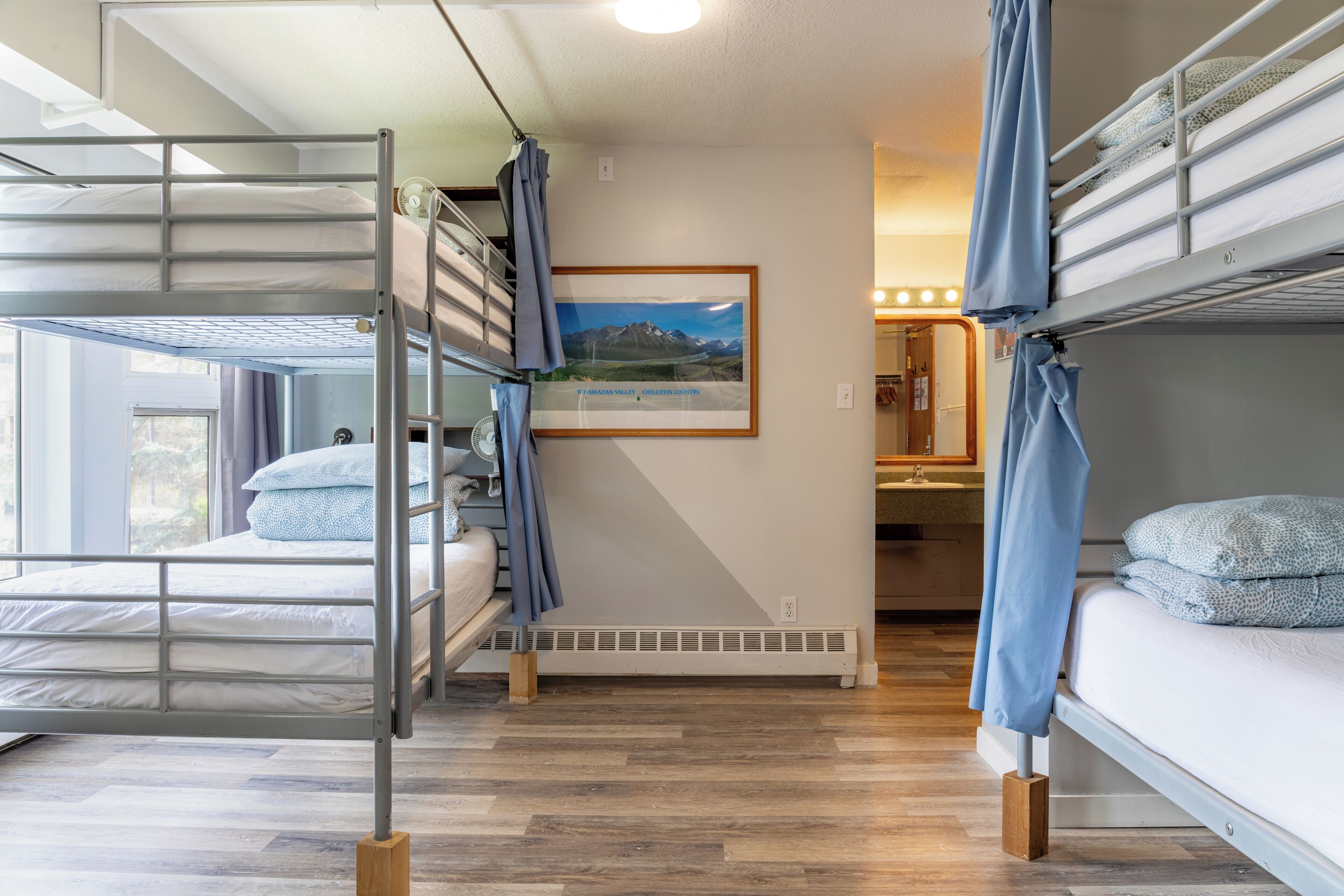 Habitación con literas, una ventana y un cuadro en la pared, además de un baño al fondo.