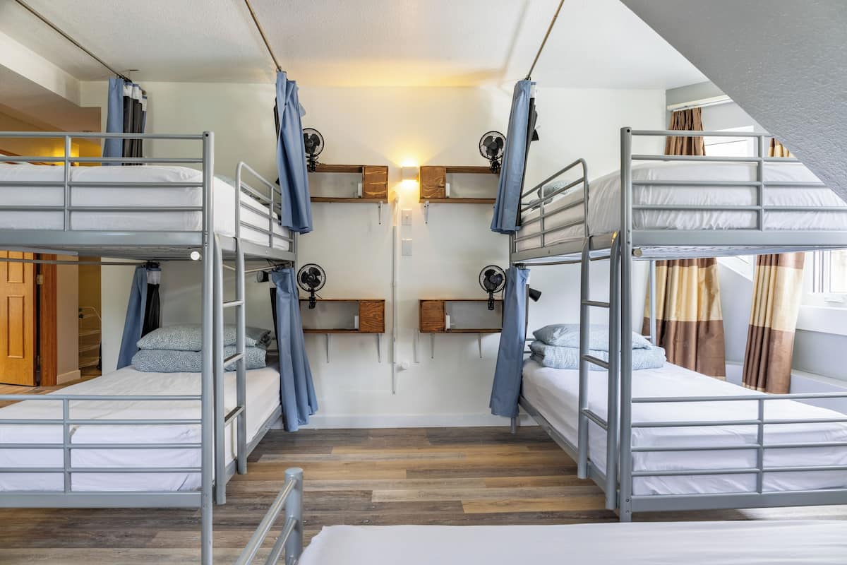 Un dormitorio con literas, suelo de madera, una luz en la pared y una ventana con cortinas.