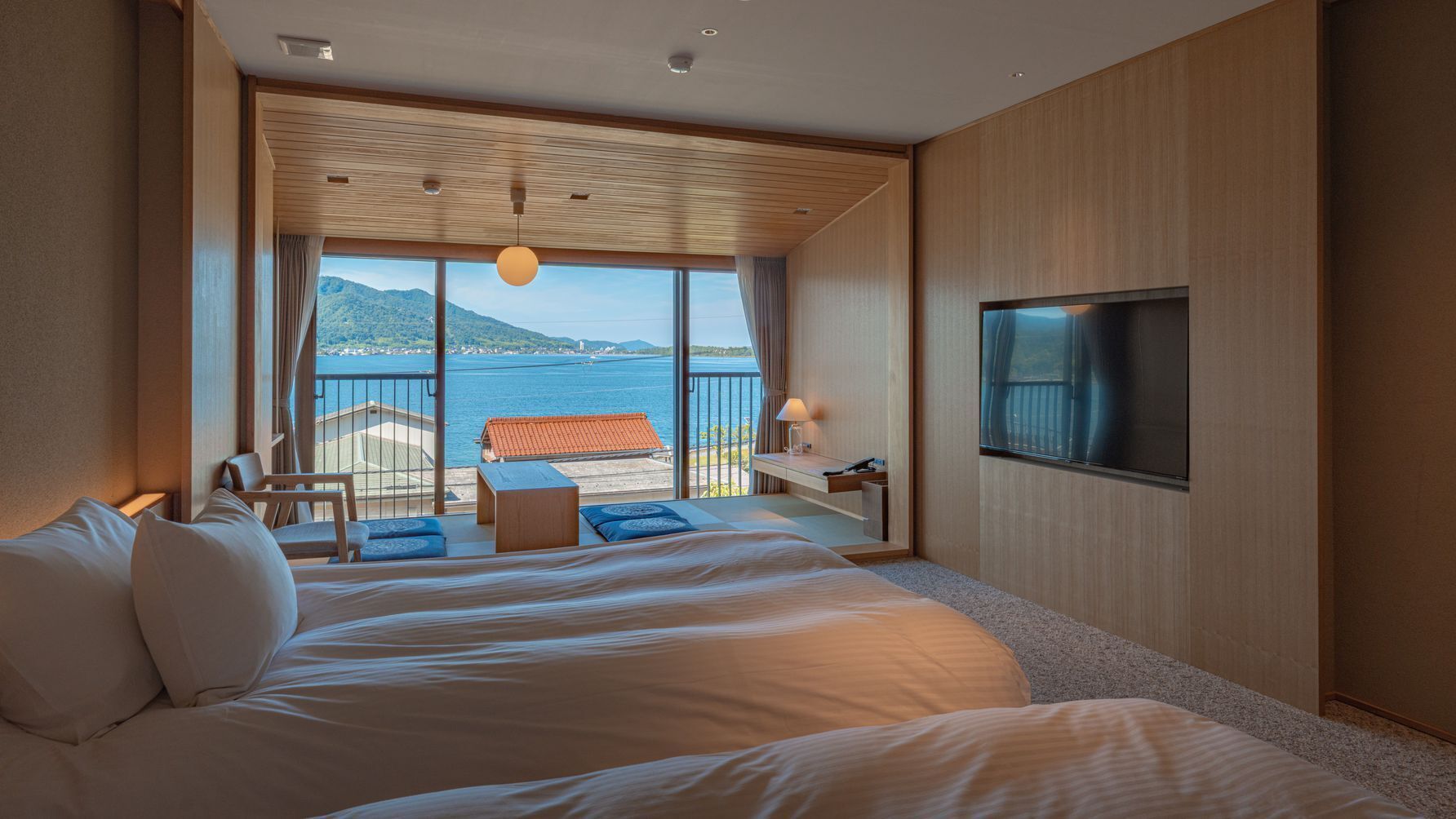 A hotel room with a large bed, a TV, a desk, and a view of the sea.