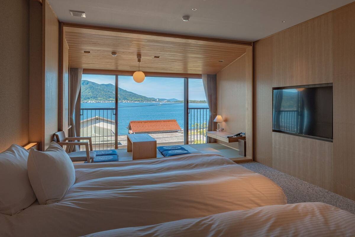 A hotel room with a large bed, a TV, a desk, and a view of the sea.
