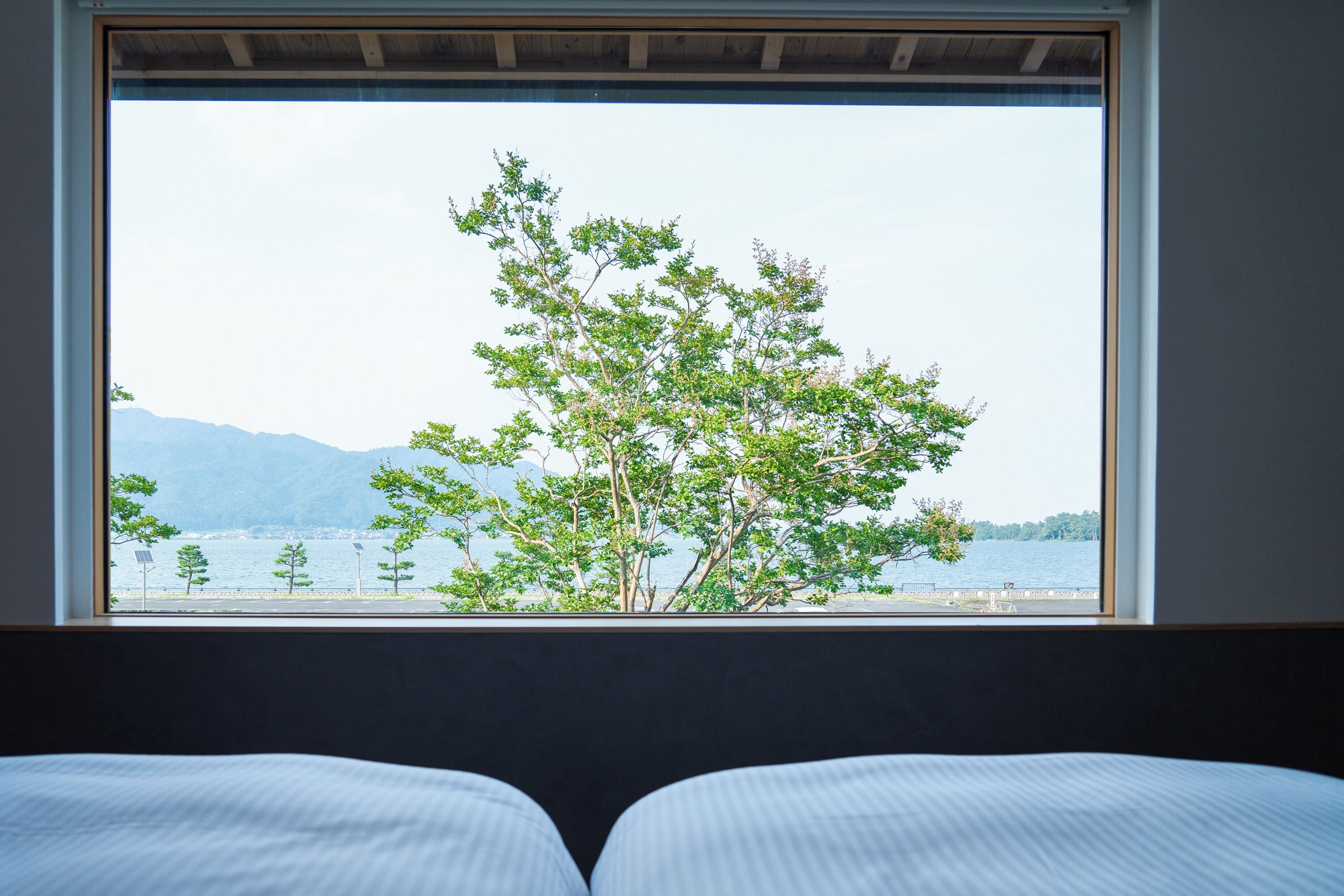 Uma cama com vista para um lago e árvores pela janela.