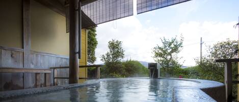A hot spring area with a wooden deck and a view of greenery and hills in the background.