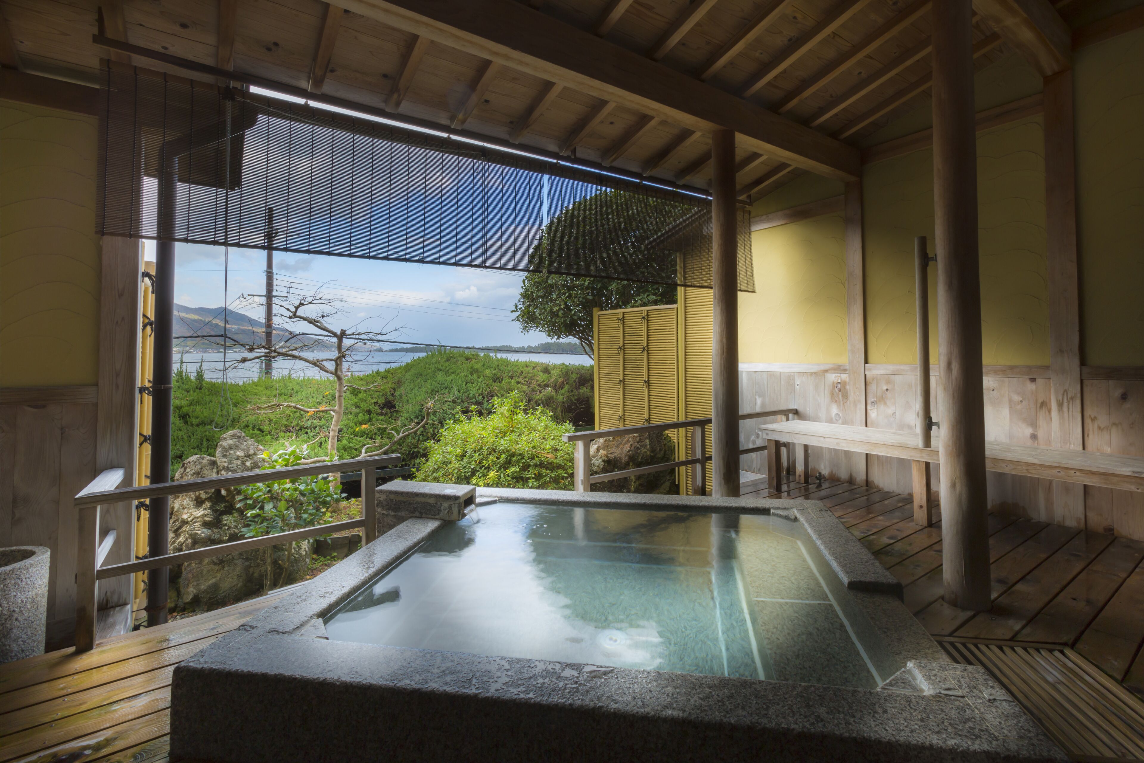A traditional Japanese onsen with a wooden deck, stone basin, and a view of a mountainous landscape.