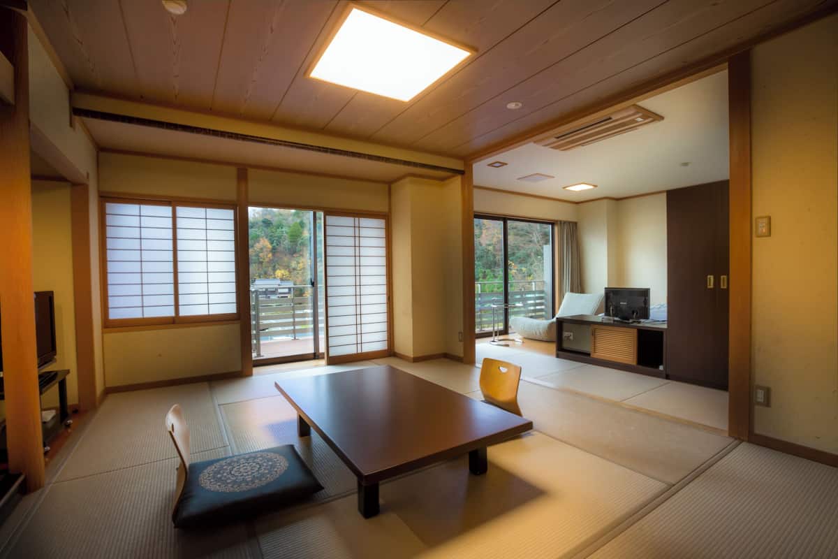 A traditional Japanese room with tatami flooring, a low table, a cushion, sliding doors, and a television.