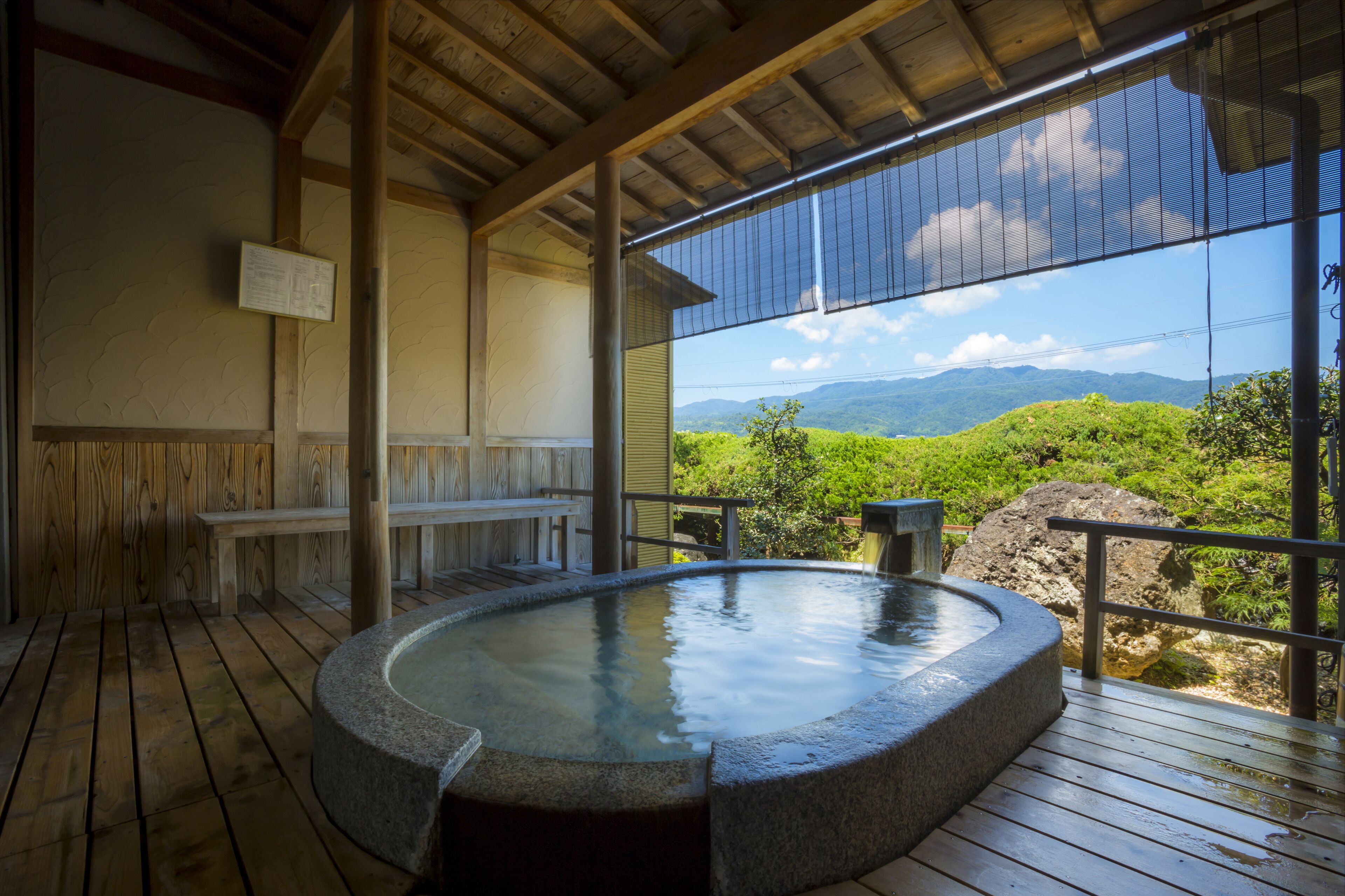 Une terrasse en bois avec un bain à remous alimenté par une source chaude, des bancs en bois et une vue sur les montagnes.