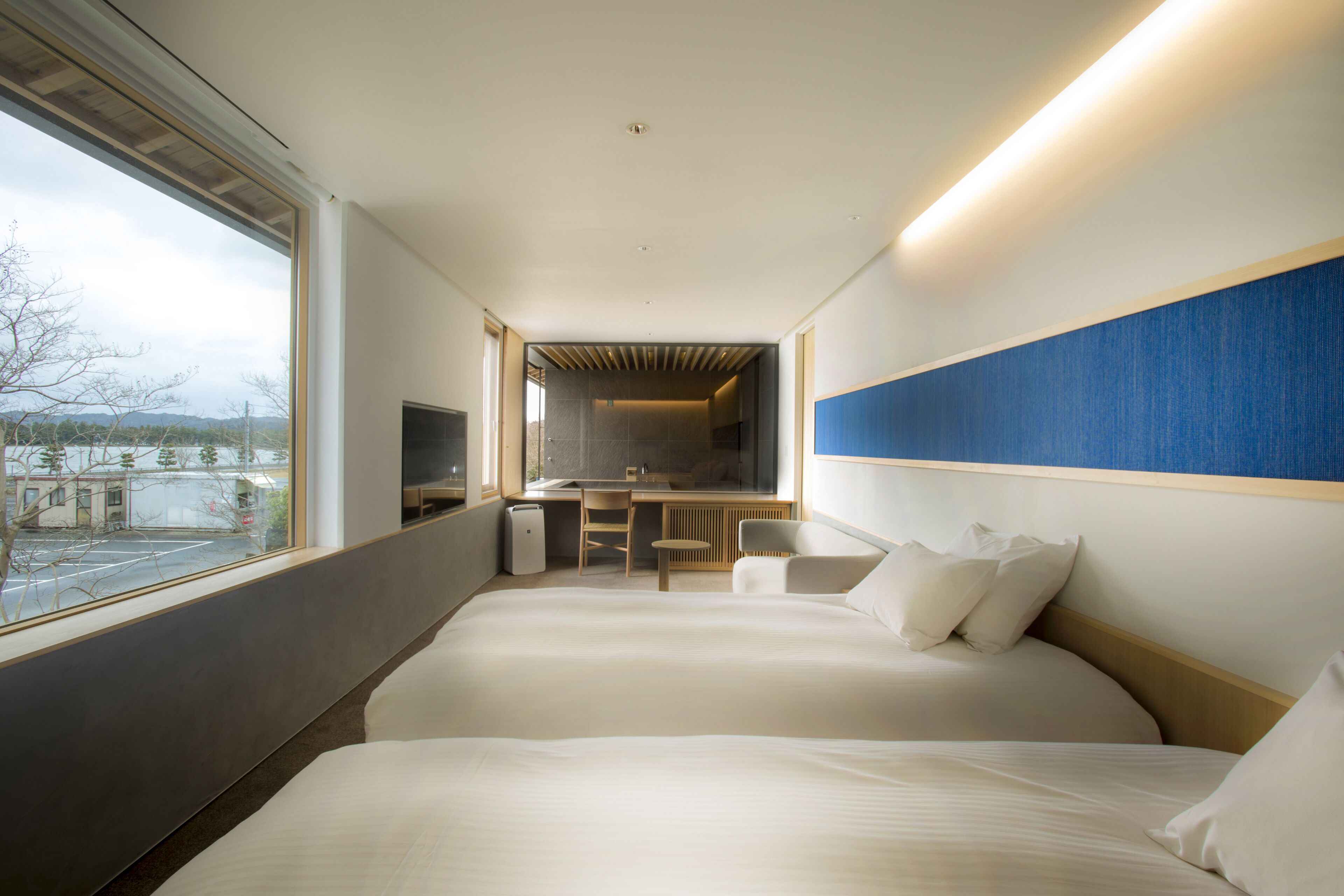 A modern hotel room with two beds, a desk, and a view of the outside.