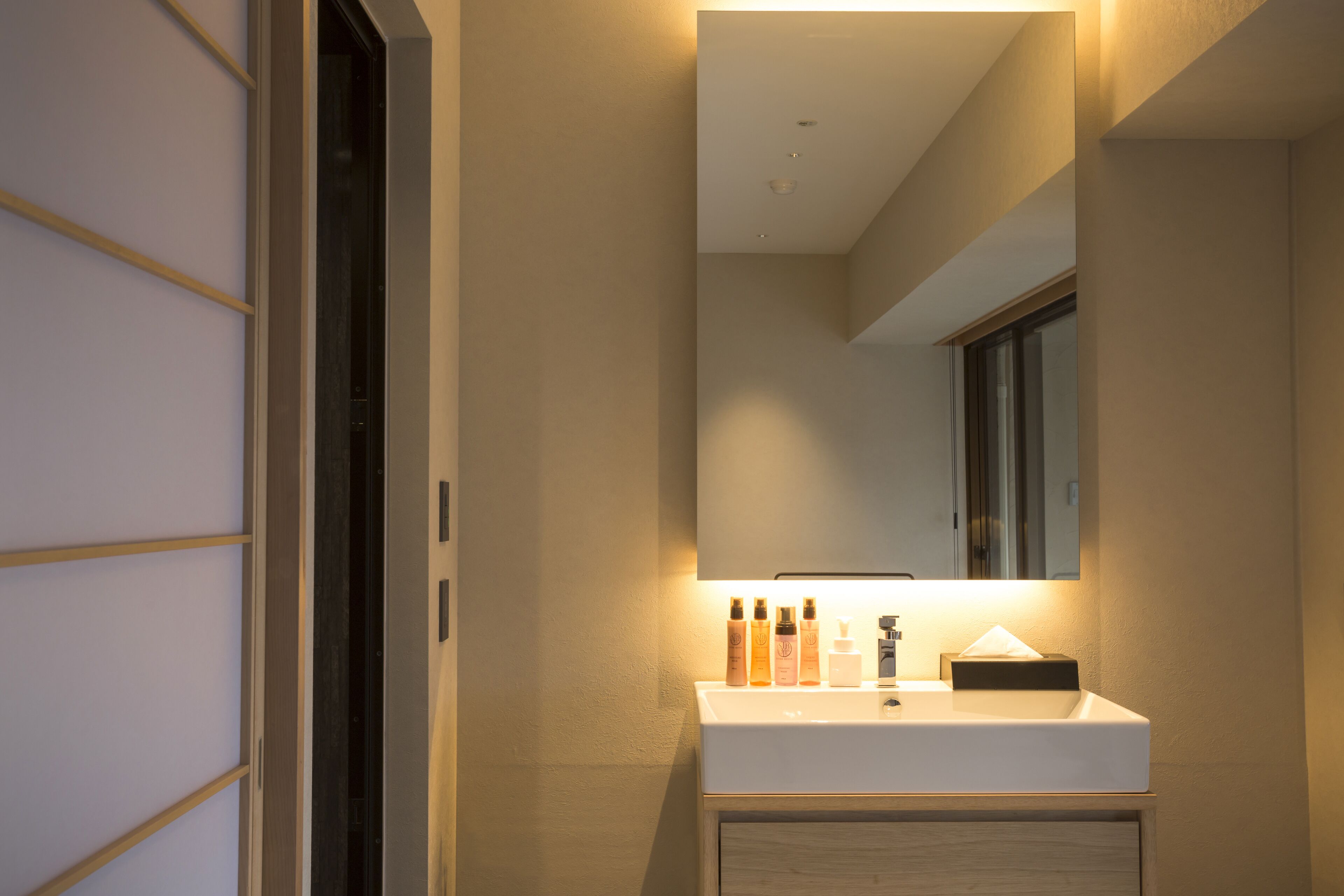 A modern bathroom with a white sink, mirror, and wooden cabinet.
