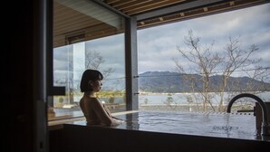 Una persona en una bañera con vista a montañas y un cuerpo de agua.