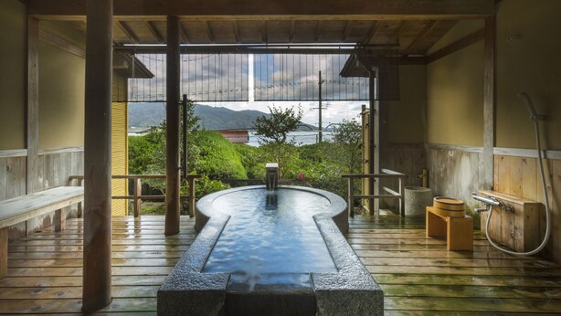 Un onsen japonés tradicional con un muelle de madera, manantial de piedra caliente y bancos de madera.