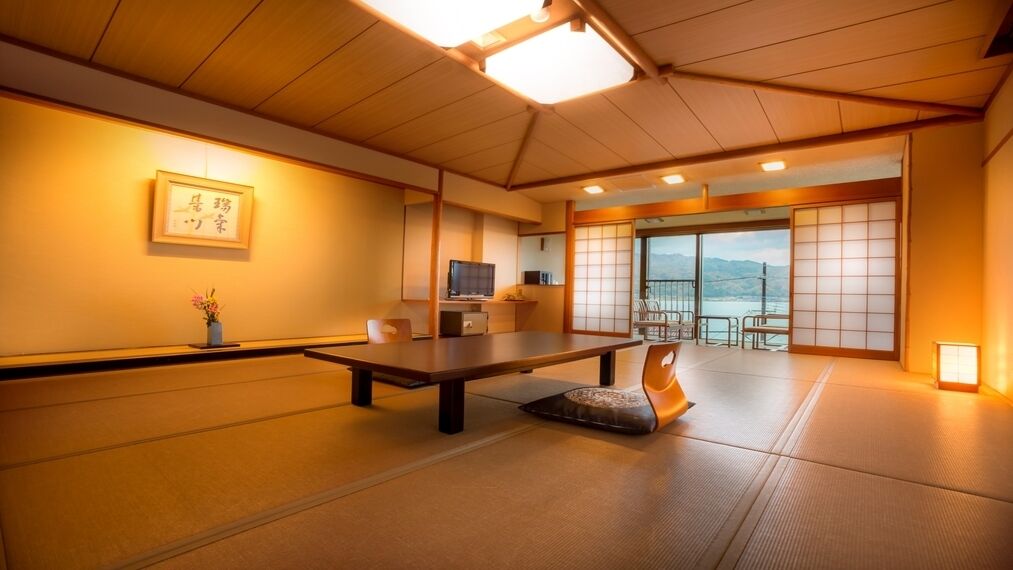 A traditional Japanese room with tatami flooring, a low table, a television, and a view of the sea.