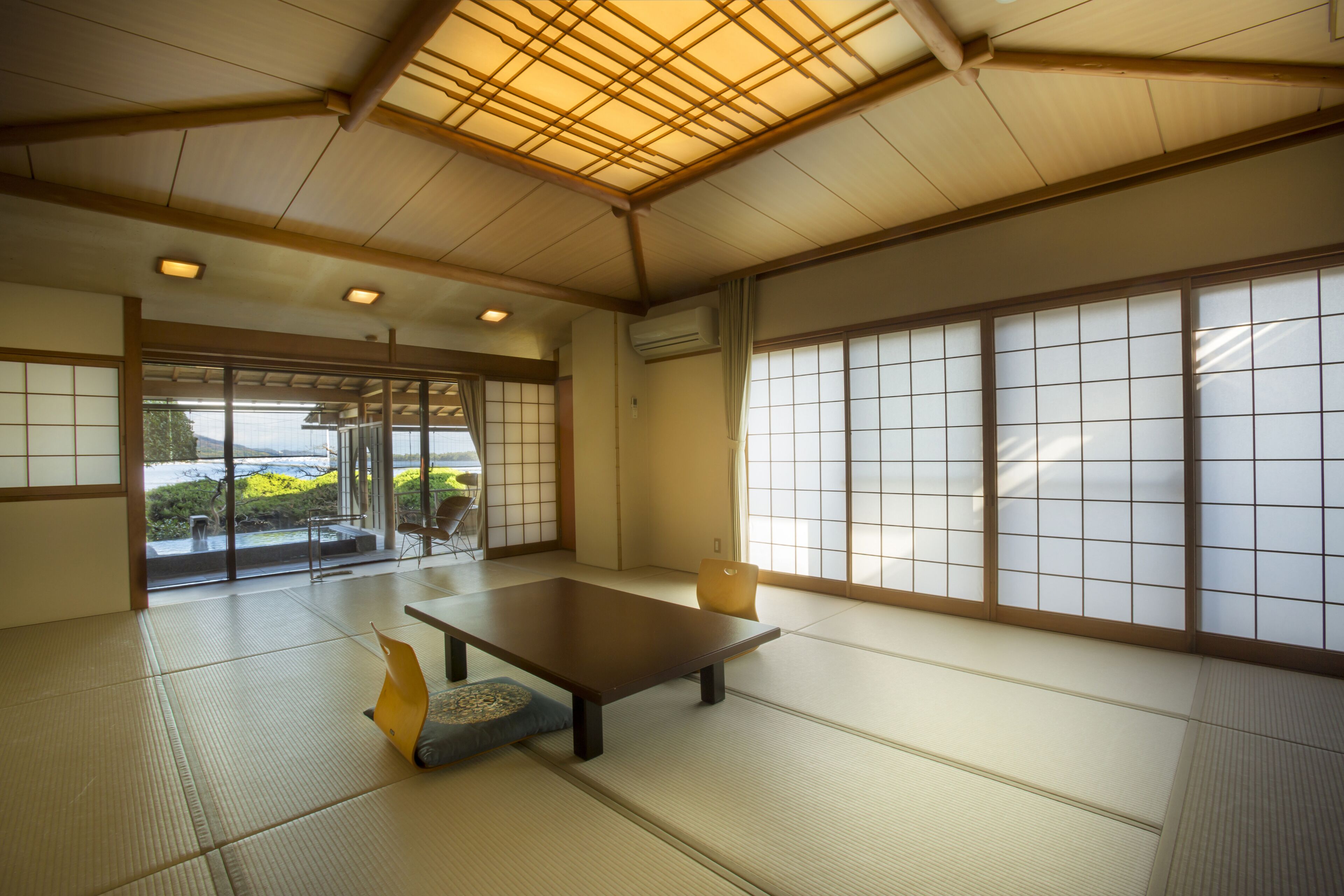 A traditional Japanese room with tatami flooring, a low table, sliding doors, and a view of a garden.