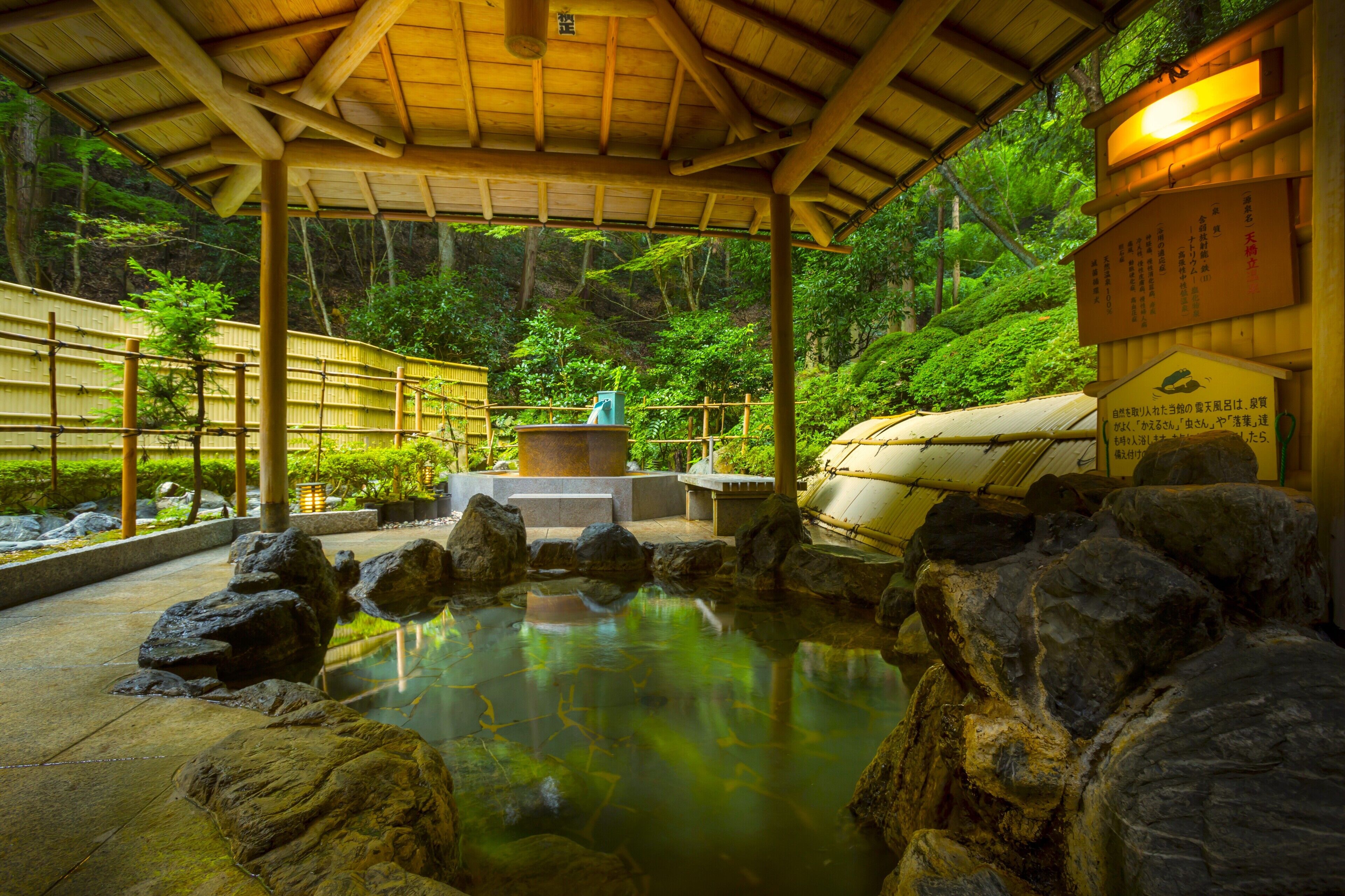 Un jardín japonés tradicional con un estanque de piedra, una valla de bambú y un pabellón de madera.