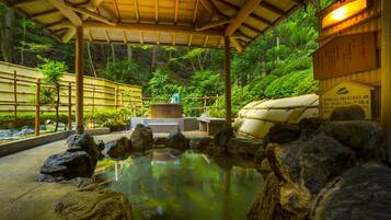 Un jardín japonés tradicional con un estanque de piedra, una valla de bambú y un pabellón de madera.