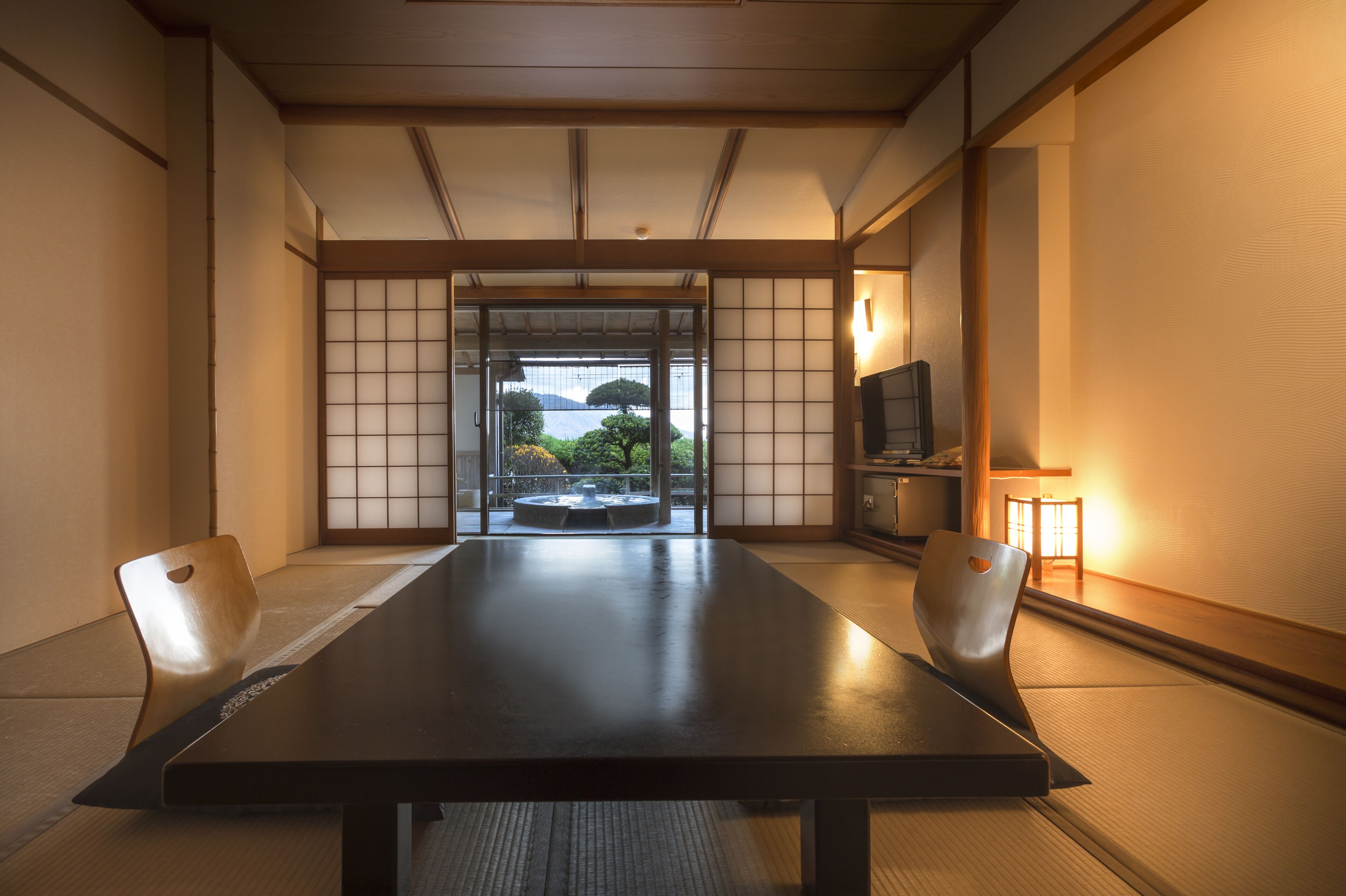 Ein traditioneller japanischer Raum mit Tatami-Bodenbelag, einem niedrigen Tisch und Schiebetüren mit Blick auf Grünflächen.