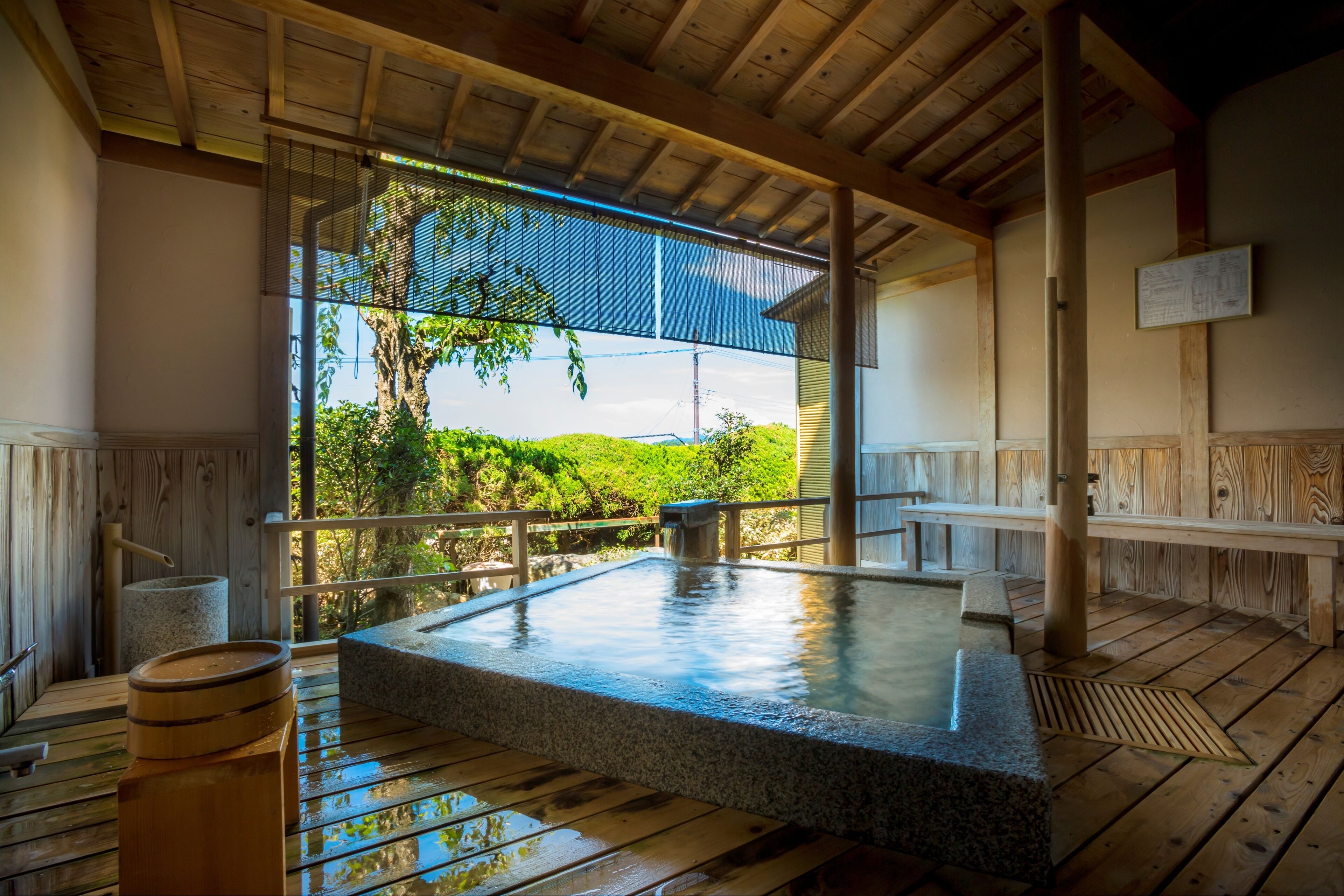A traditional Japanese onsen with a stone hot spring, wooden deck, and a view of lush greenery.