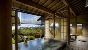 Un onsen japonés tradicional con una terraza de madera, una fuente termal de piedra y vistas del paisaje circundante.