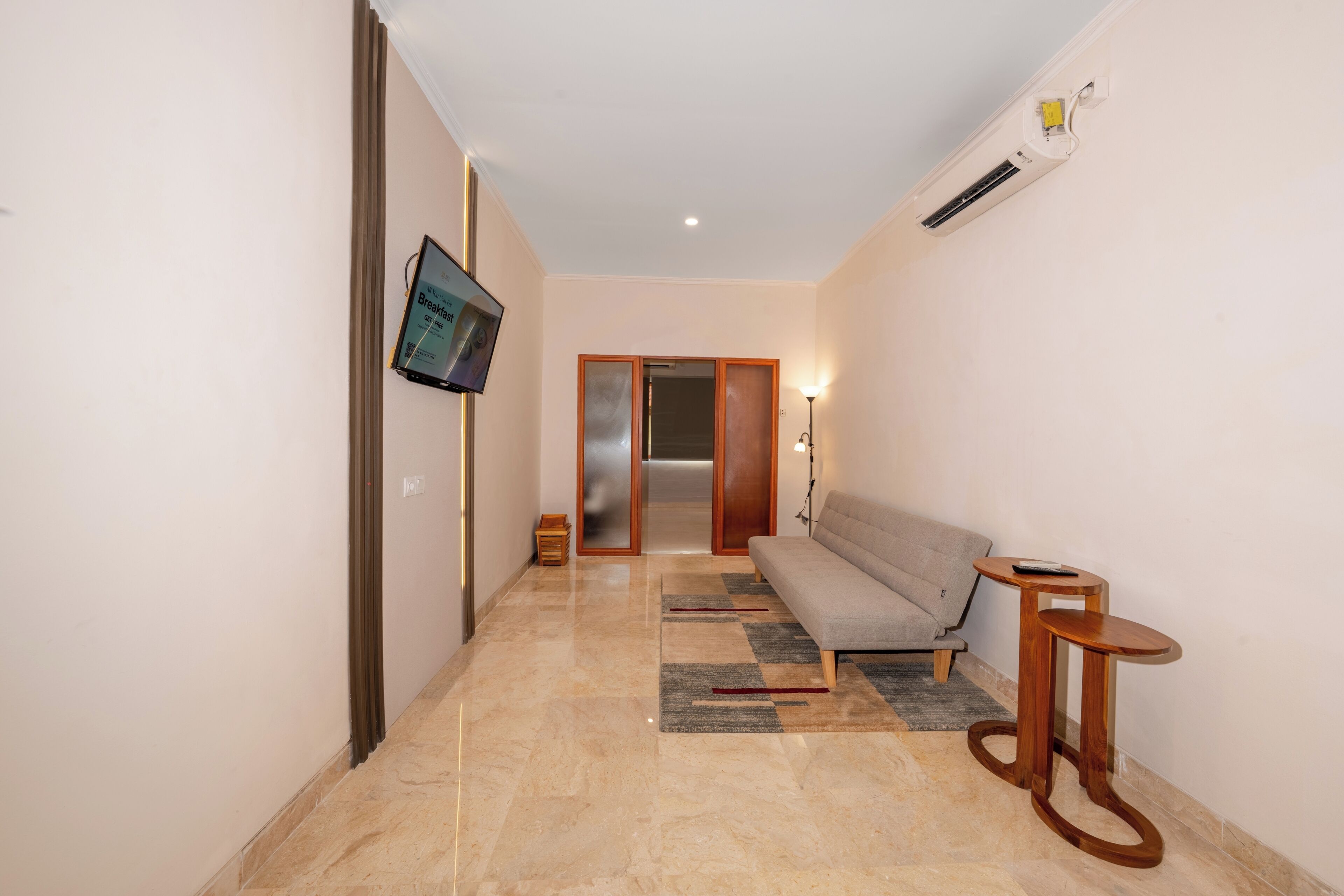A hallway with a sofa, a small table, a TV mounted on the wall, and a door leading to another room.