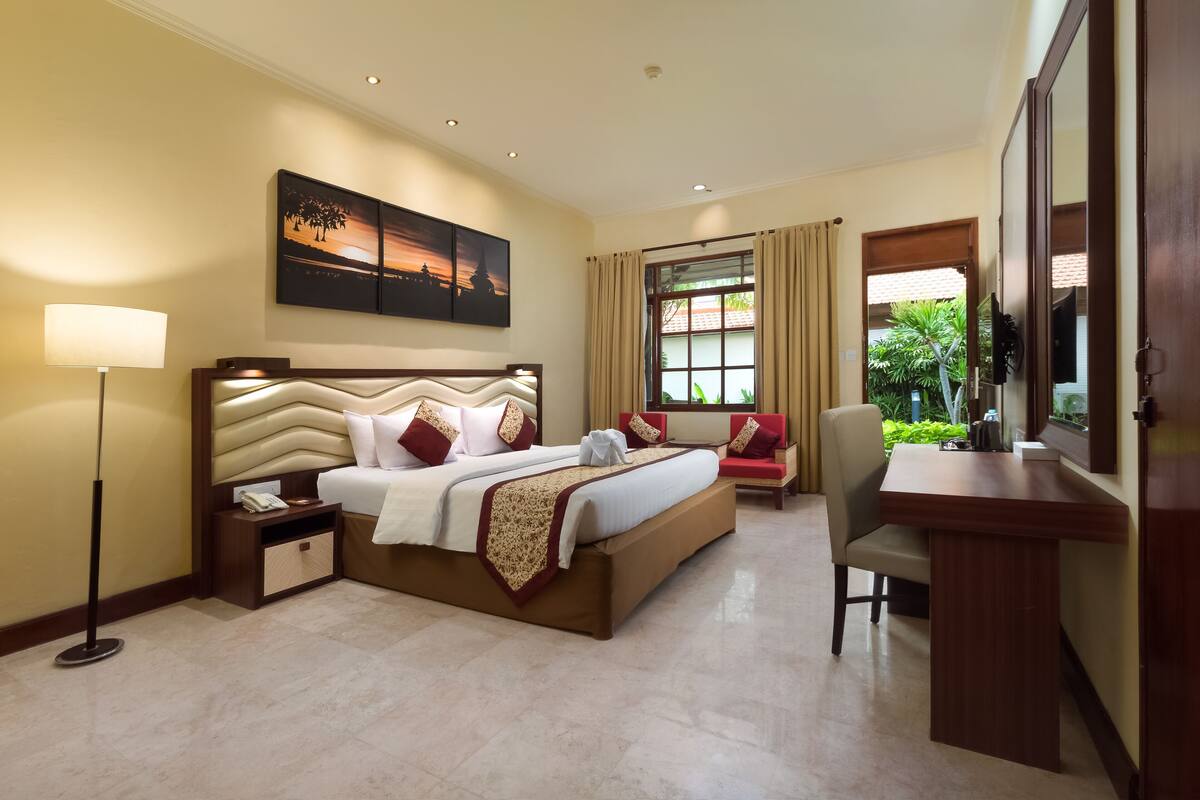 A hotel room with a bed, bedside table, lamp, desk, chair, and a large window with curtains.