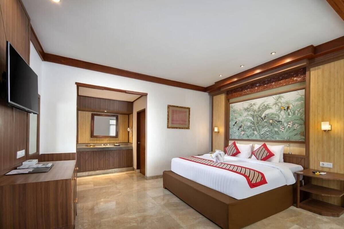A hotel room with a large bed, a desk, a television, a bathroom, and a large painting on the wall.