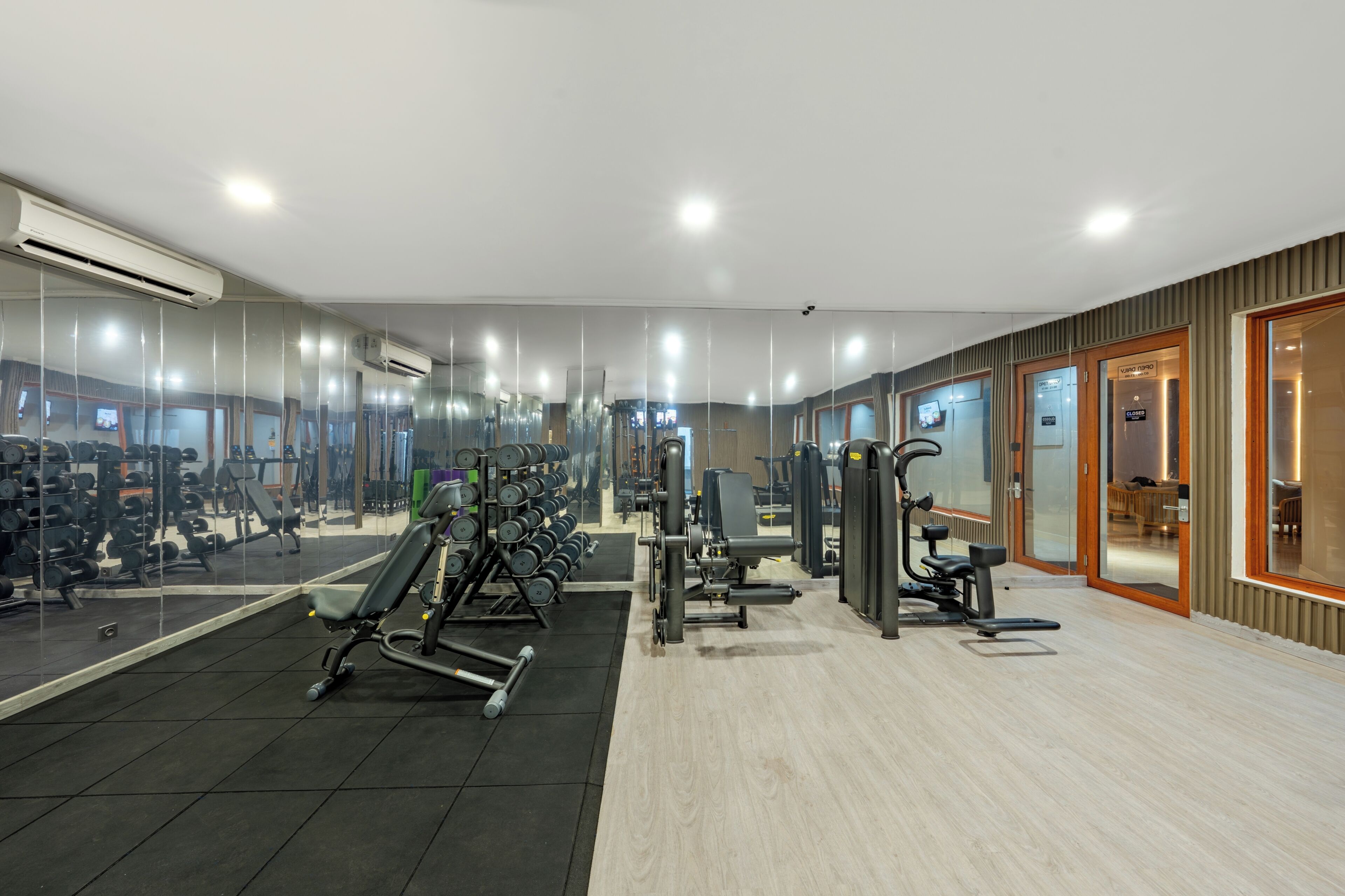 A gym with mirrored walls, various exercise equipment, and a wooden floor.