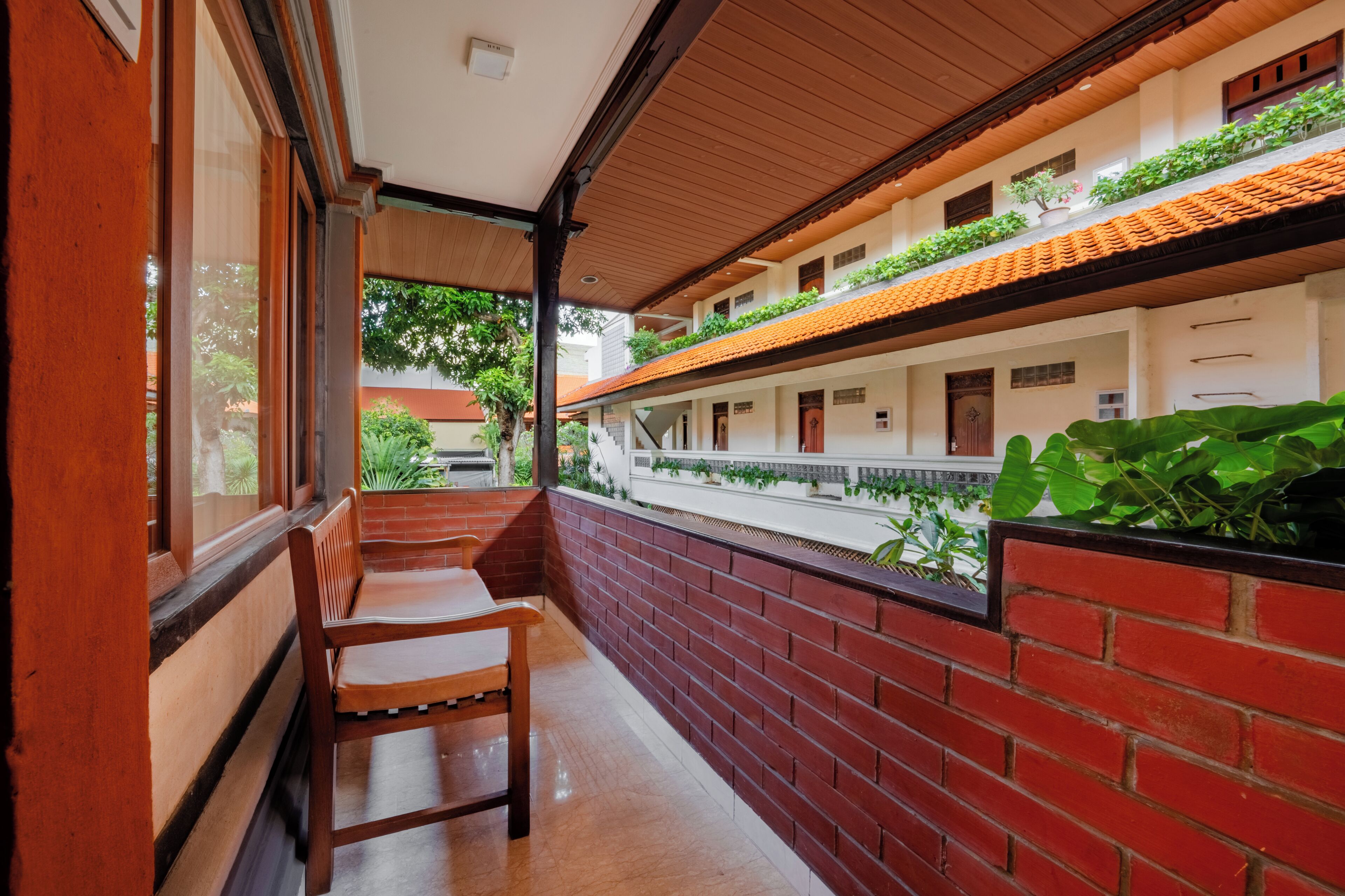 A corridor with a wooden bench, brick walls, and a view of greenery outside.