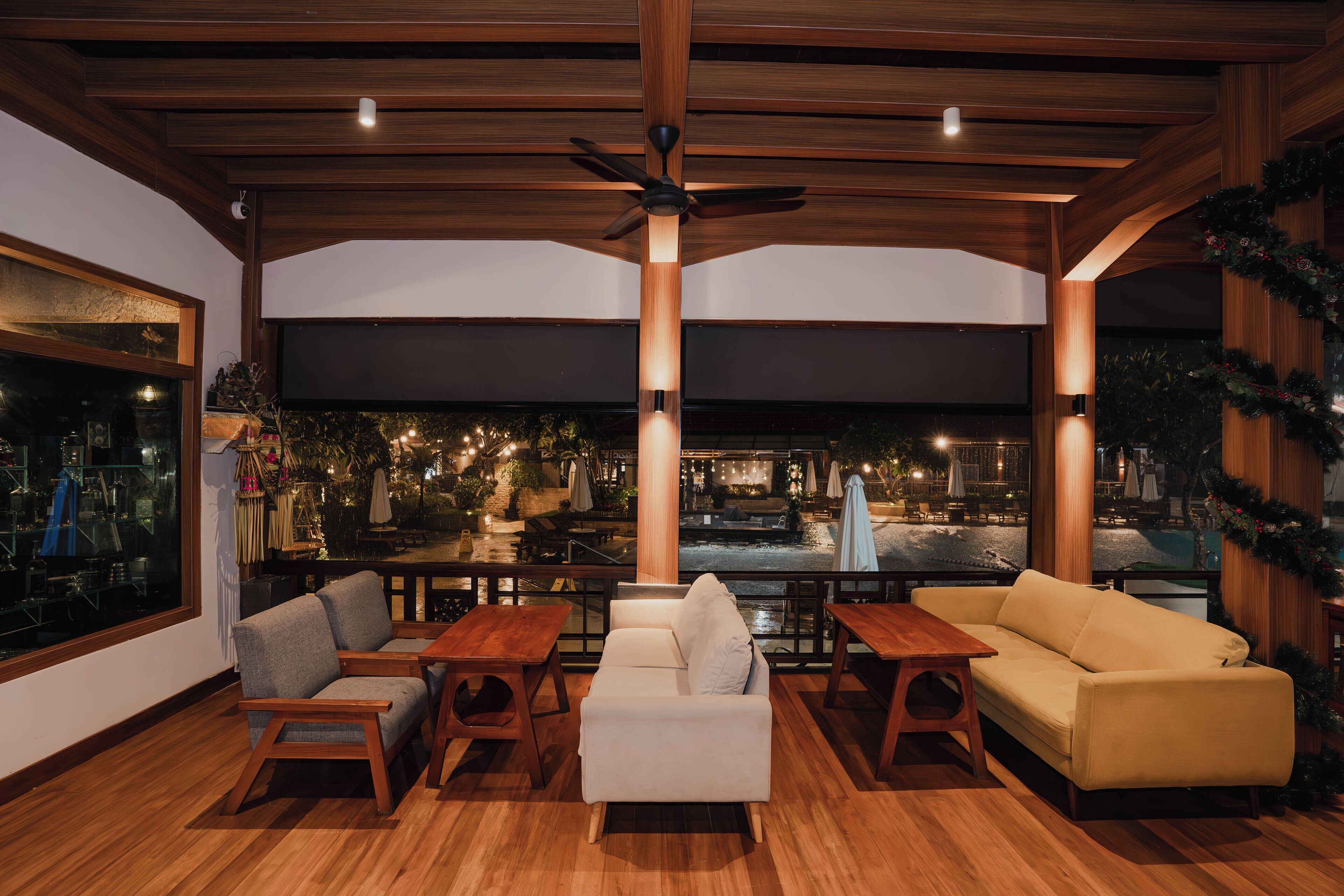 Un rincón de sala acogedor con techo de madera, ventilador de techo y vistas a un patio exterior con mesas y sillas.