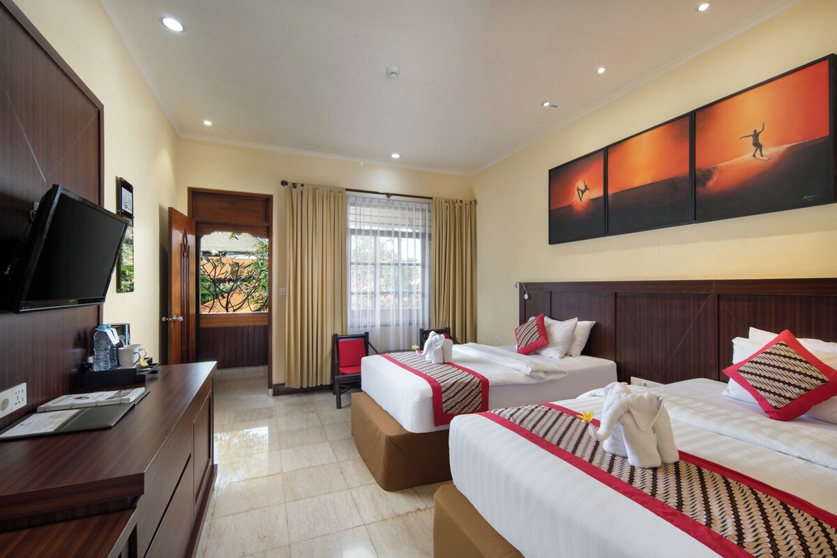 A hotel room with two beds, a desk, a television, and a large window with curtains.