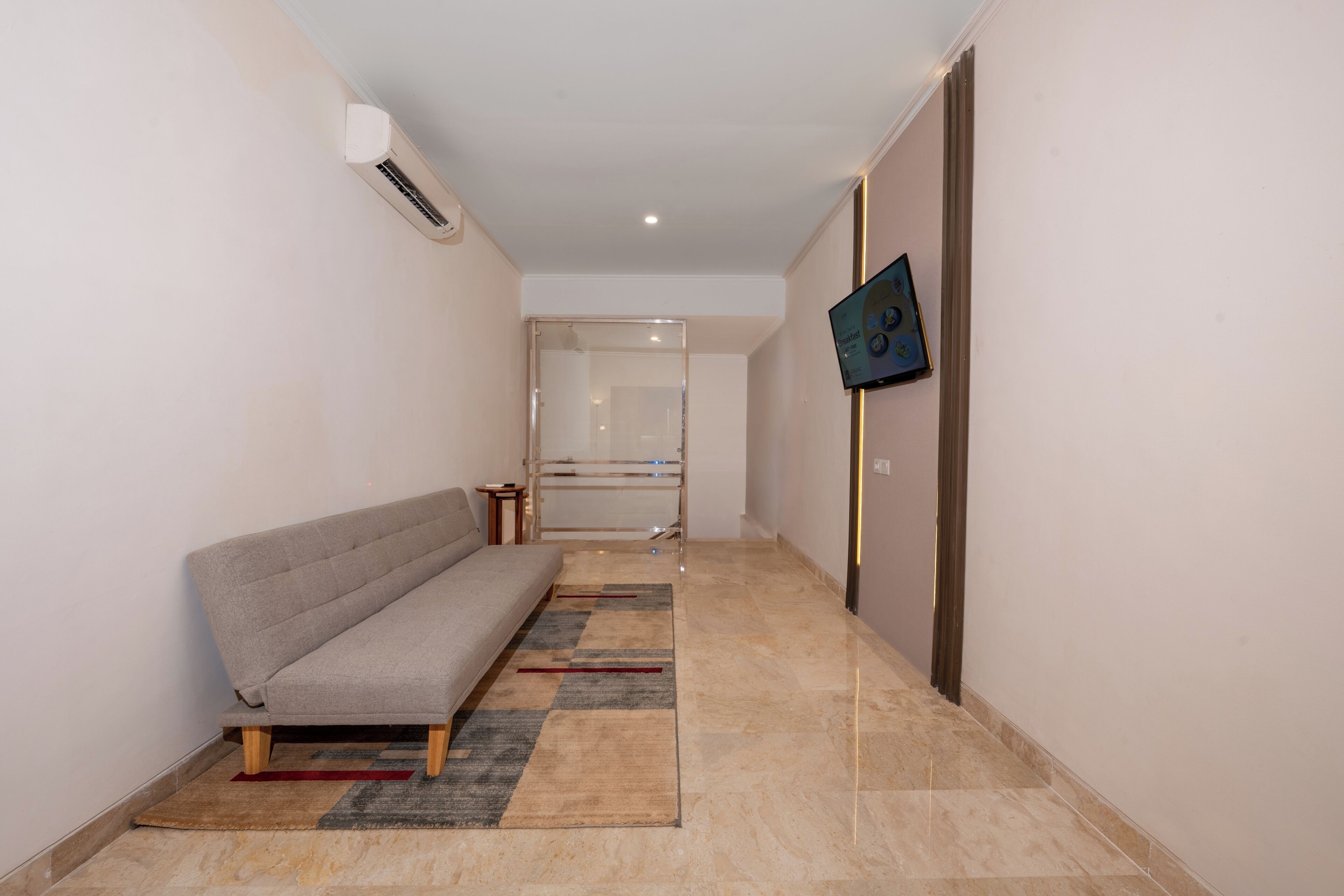 A hallway with a sofa, a TV mounted on the wall, and a glass door leading to another room.