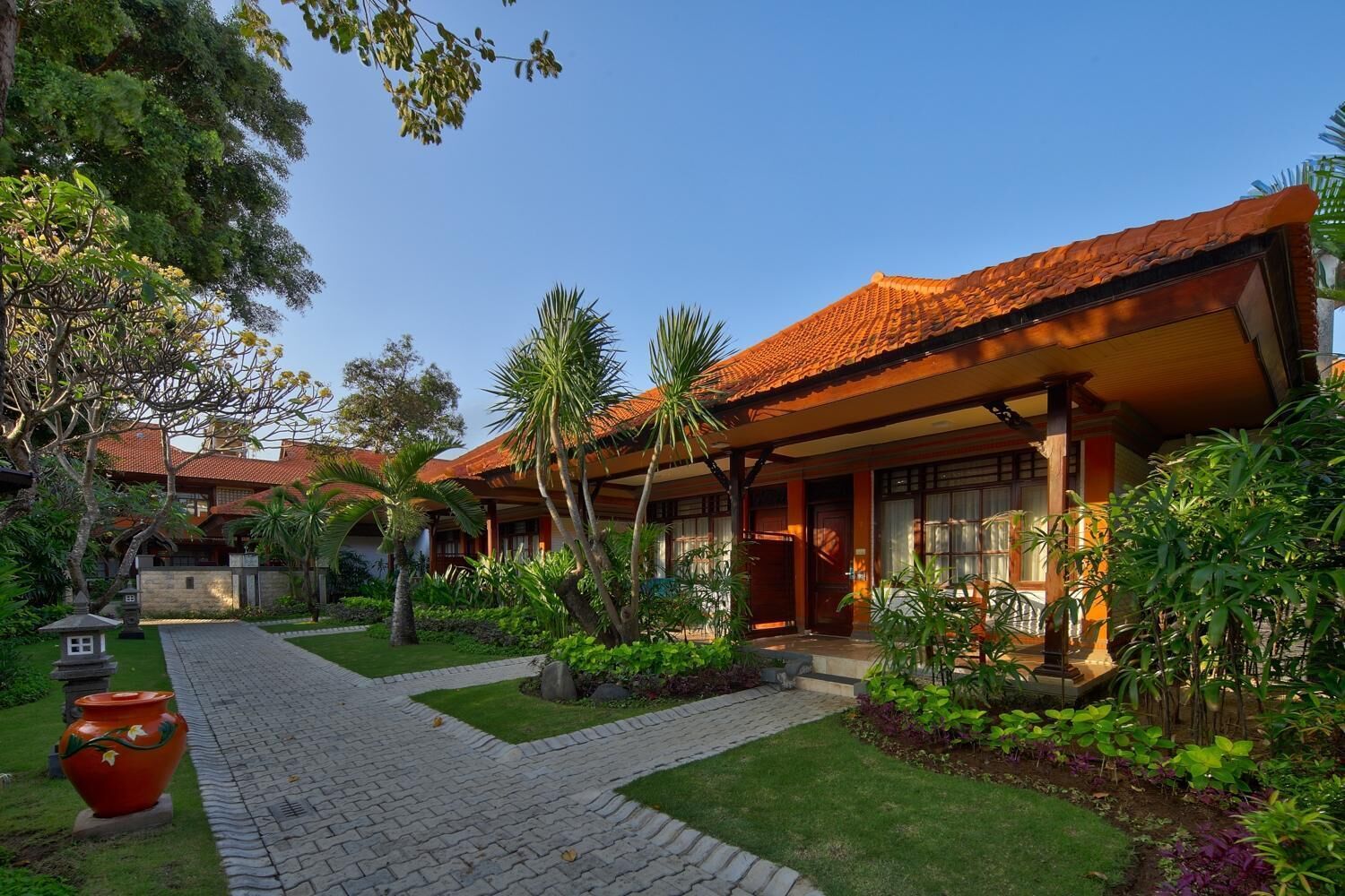 A traditional house with a tiled roof, surrounded by lush greenery and a paved pathway.