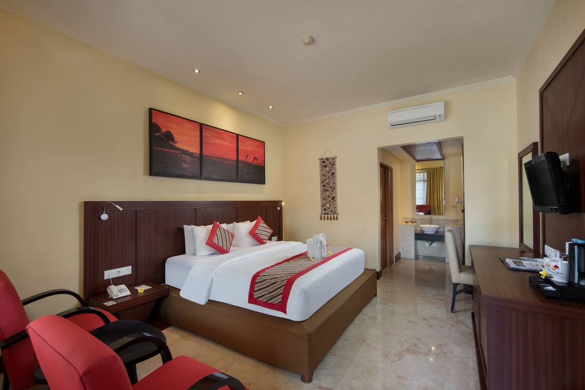 A hotel room with a large bed, a desk, a chair, a TV, and a bathroom visible through an open door.