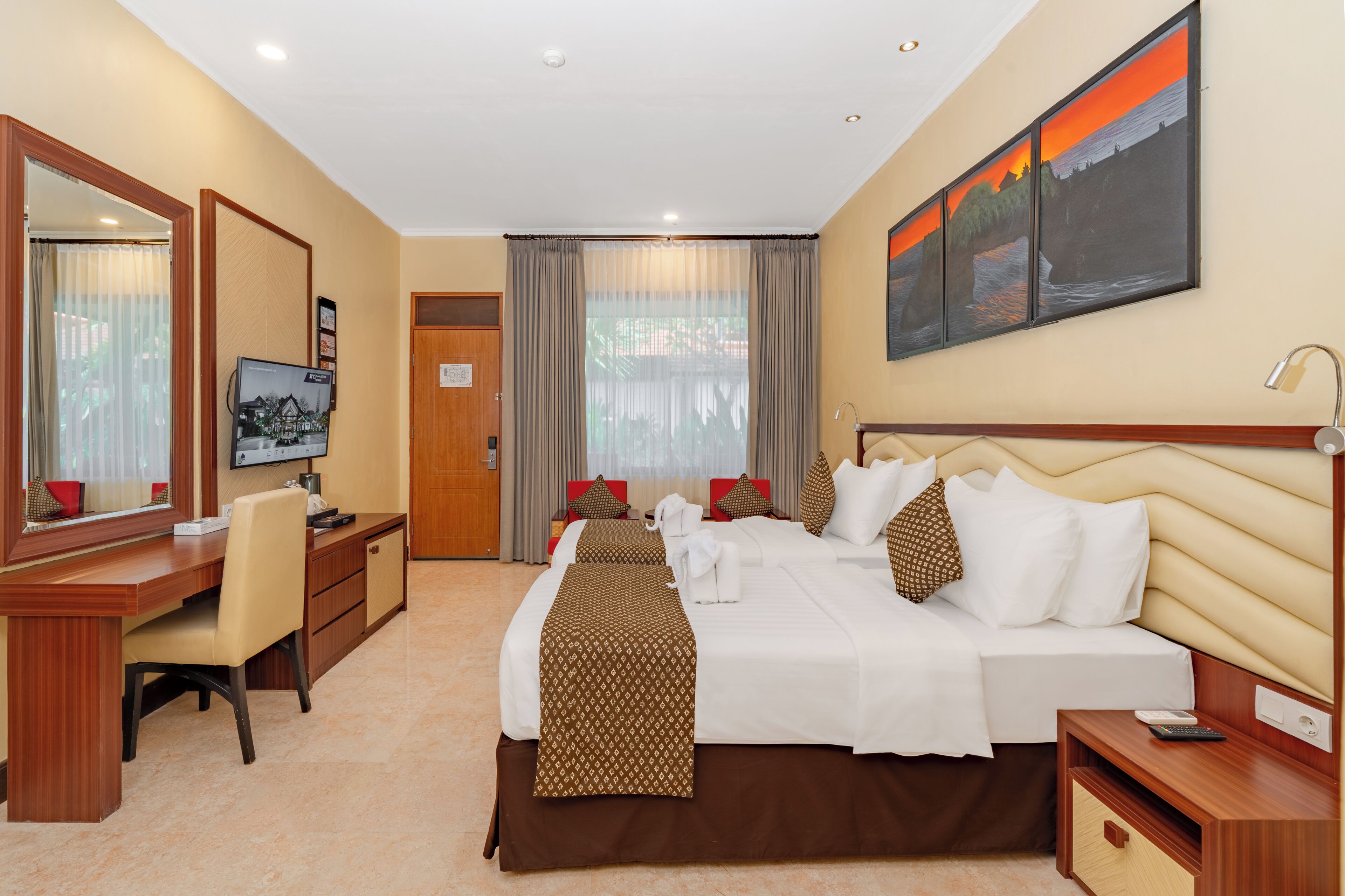 Quarto de hotel com uma cama, escrivaninha, cadeira, televisão e um quadro na parede.