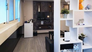 Habitación de hotel moderna con televisor de pantalla plana, refrigerador pequeño, cafetera, planta en maceta y estante con artículos de tocador.