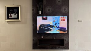Una sala de estar moderna con un televisor de pantalla plana montado en la pared, una obra de arte enmarcada encima y un pequeño estante con objetos decorativos.